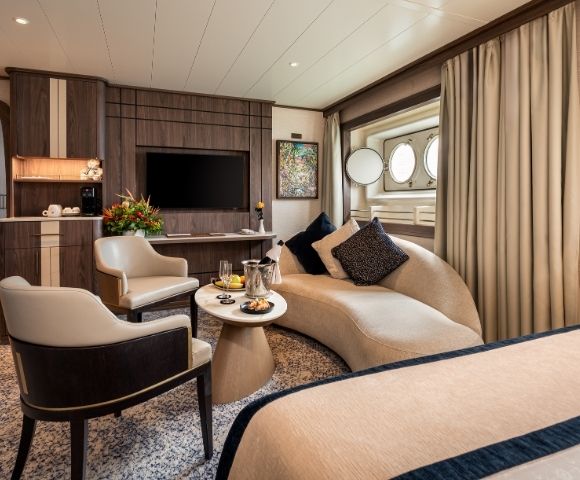 Spacious cruise ship suite with seating area, large windows, and modern furnishings.