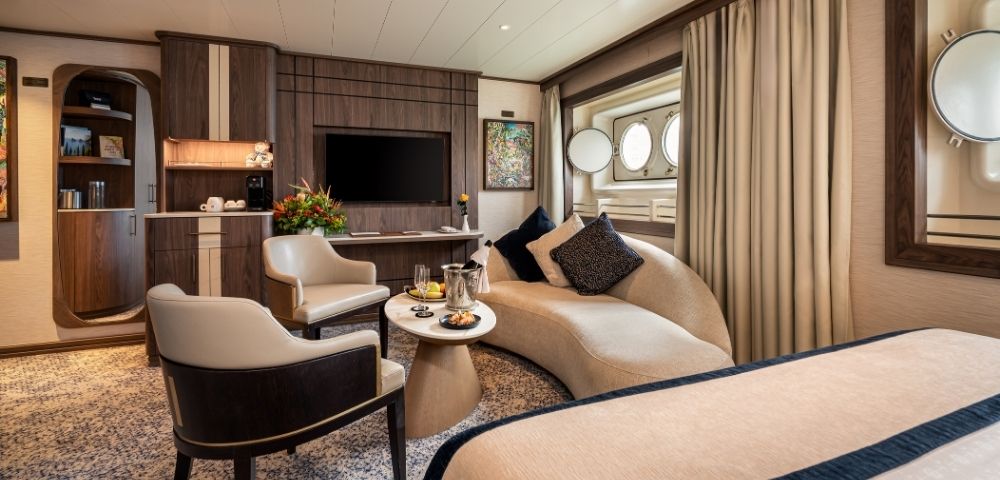 Spacious cruise ship suite with seating area, large windows, and modern furnishings.