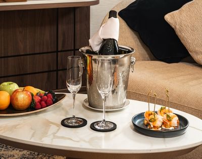 Suite welcome amenities including fruit, champagne, and snacks on a coffee table.