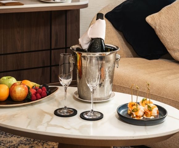 Suite welcome amenities including fruit, champagne, and snacks on a coffee table.