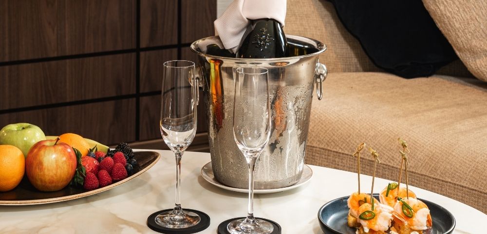 Suite welcome amenities including fruit, champagne, and snacks on a coffee table.