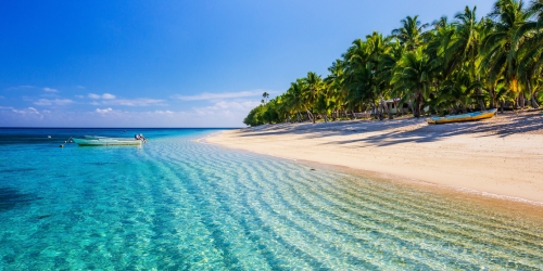Tropical beach with clear turquoise water, white sand, palm trees, and a small boat under a bright blue sky, creating a peaceful paradise.