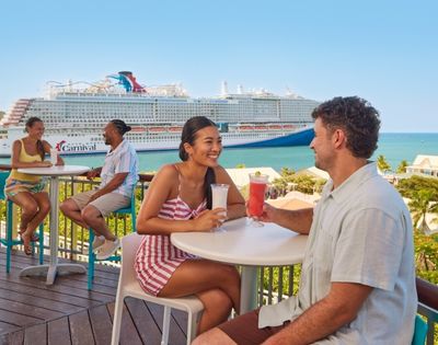 Guests enjoying drinks and conversation on an outdoor cruise ship deck overlooking the ocean.