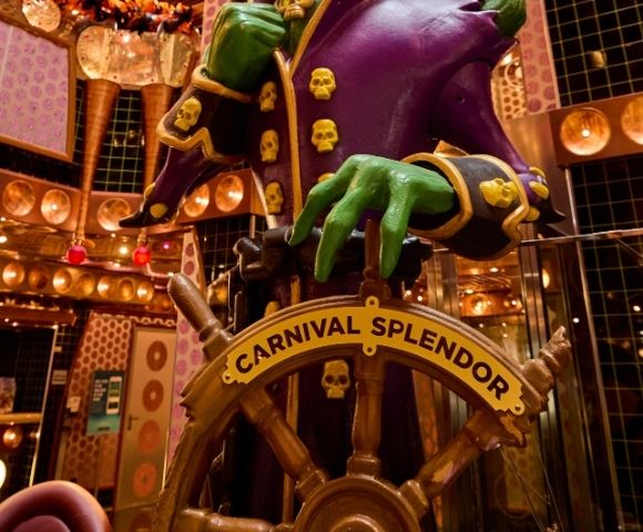 Colorful atrium centerpiece sculpture surrounded by multiple decks and decorative lighting aboard a cruise ship.