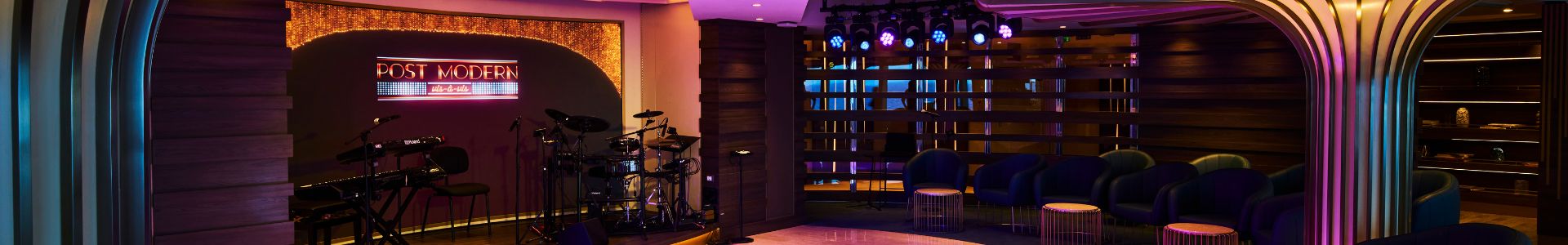 Stage area with a drum kit, keyboard, and neon sign reading 