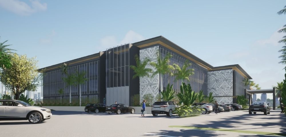 A modern architectural rendering of a multi-story office building with dark gray and white patterned facade elements, a dark roof with gold trim, and extensive floor-to-ceiling windows, set amidst lush palm trees and tropical foliage, with a paved parking lot in the foreground containing several parked cars.