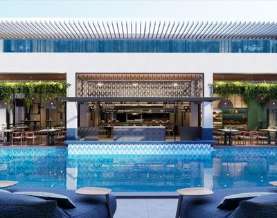 A modern hotel pool area with a bar and dining space overlooking the water, featuring green plants and stylish seating.