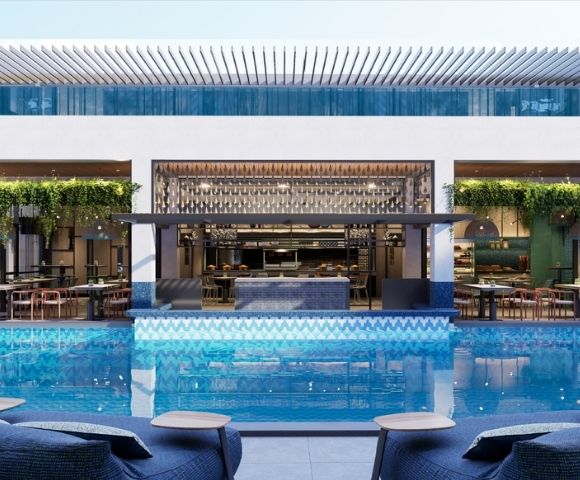 A modern hotel pool area with a bar and dining space overlooking the water, featuring green plants and stylish seating.
