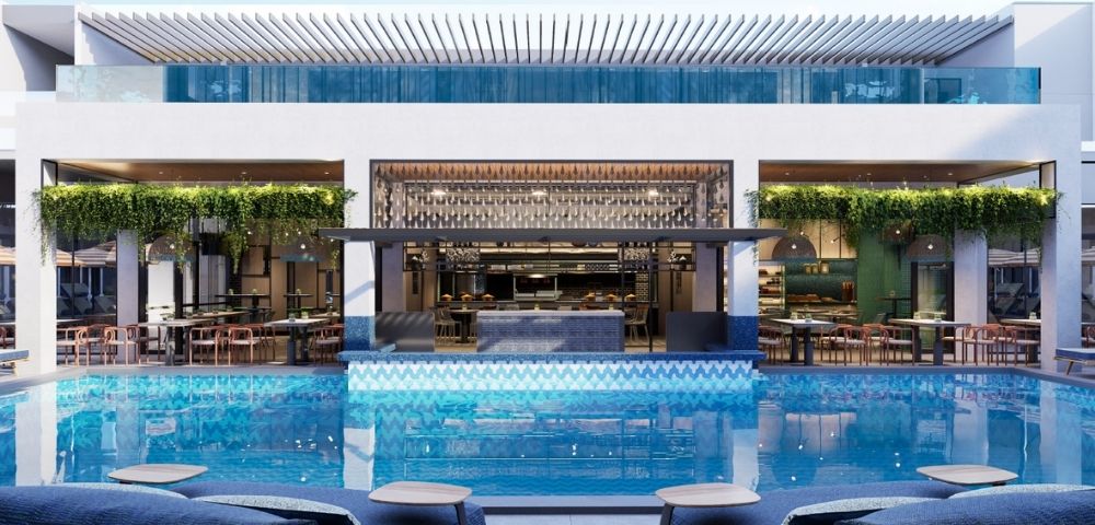 A modern hotel pool area with a bar and dining space overlooking the water, featuring green plants and stylish seating.