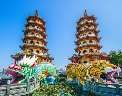 Colorful dragon and tiger towers with intricate designs next to a body of water under a clear blue sky.