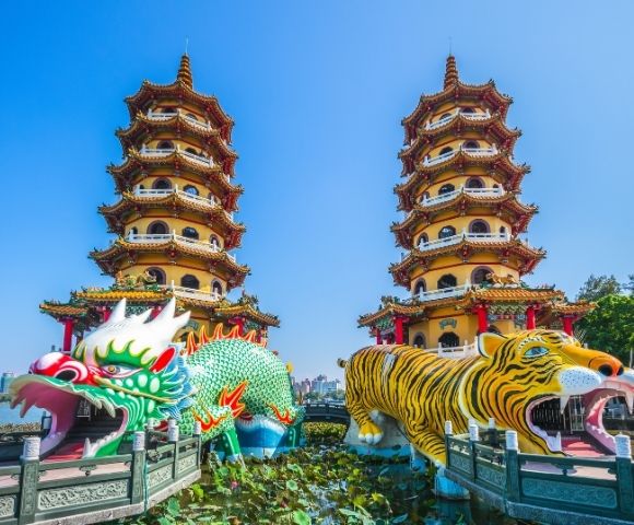 Colorful dragon and tiger towers with intricate designs next to a body of water under a clear blue sky.