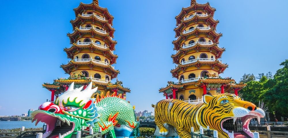 Colorful dragon and tiger towers with intricate designs next to a body of water under a clear blue sky.