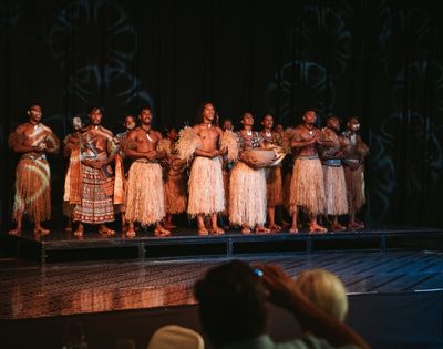 A group of performers dressed in traditional attire with grass skirts, standing on a stage, showcasing a cultural dance or performance.