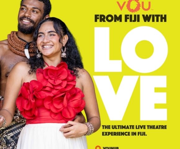A couple dressed in traditional Fijian attire, with the woman wearing a red dress adorned with large flowers, smiling against a bright yellow background featuring the text 