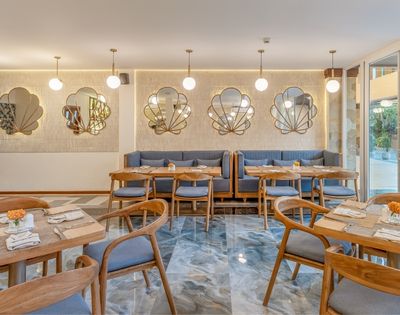 An elegant restaurant interior with marble flooring, booth seating, wooden tables and chairs, and decorative shell-shaped mirrors on a textured wall.