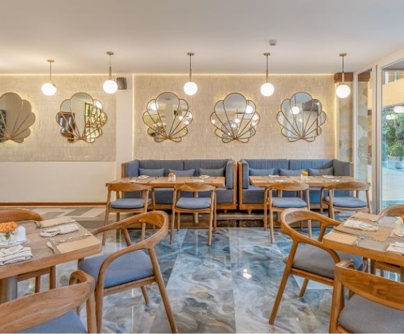 An elegant restaurant interior with marble flooring, booth seating, wooden tables and chairs, and decorative shell-shaped mirrors on a textured wall.