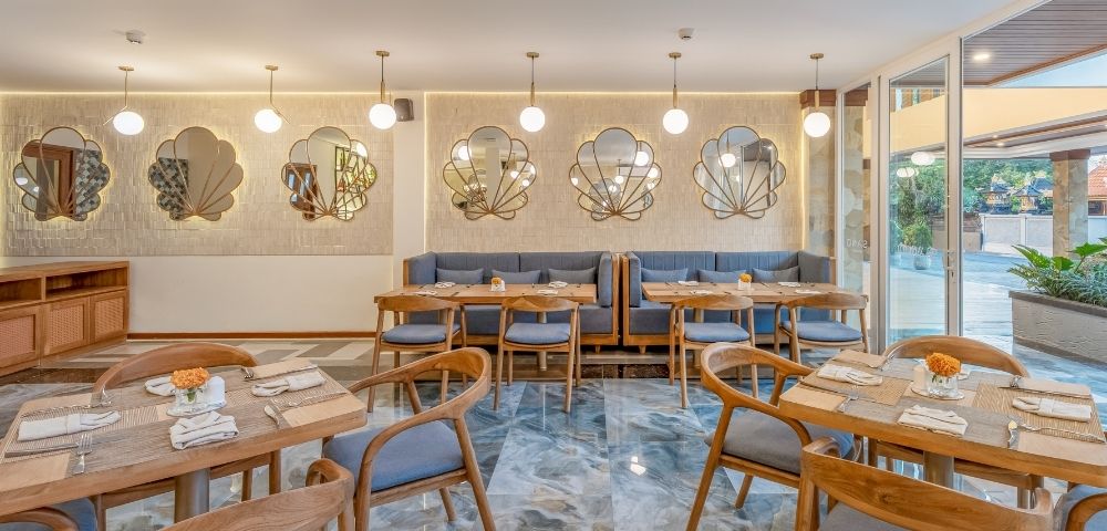 An elegant restaurant interior with marble flooring, booth seating, wooden tables and chairs, and decorative shell-shaped mirrors on a textured wall.