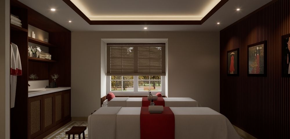 A serene spa treatment room with two massage tables, each adorned with red runners and white towels, bathed in soft, indirect ceiling lighting.