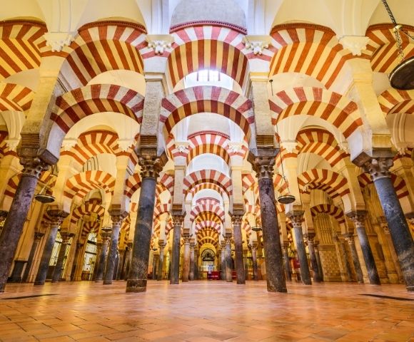 Interior of the Great Mosque of Córdoba, featuring multiple arches with red and white striped patterns and columns.