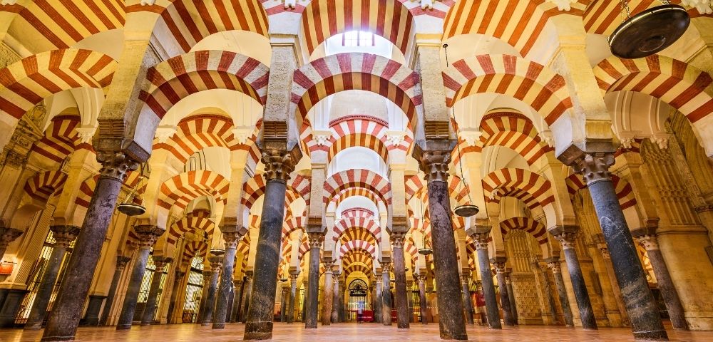 Interior of the Great Mosque of Córdoba, featuring multiple arches with red and white striped patterns and columns.