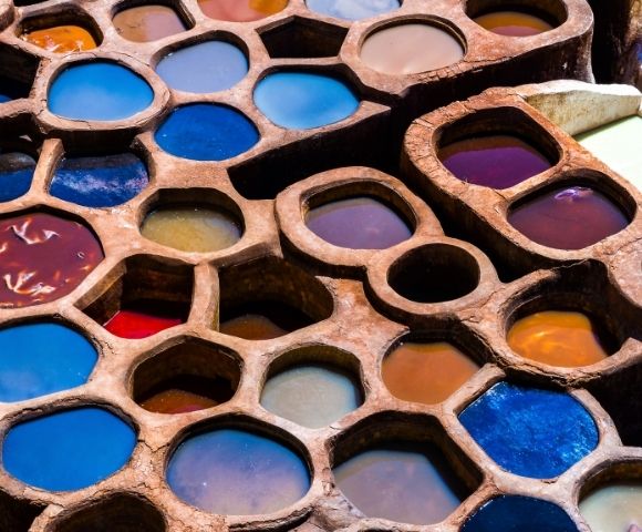 A close-up view of circular dye pits filled with vibrant colored liquids, arranged in a honeycomb pattern.