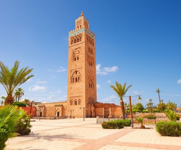 Koutoubia Mosque in Marrakech, Morocco, with a clear blue sky and palm trees in the foreground.