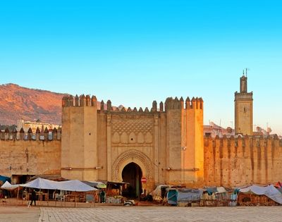A historical gate of a fortified city with stone walls, surrounded by a market area.
