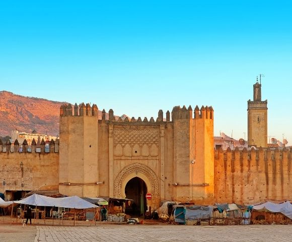 A historical gate of a fortified city with stone walls, surrounded by a market area.