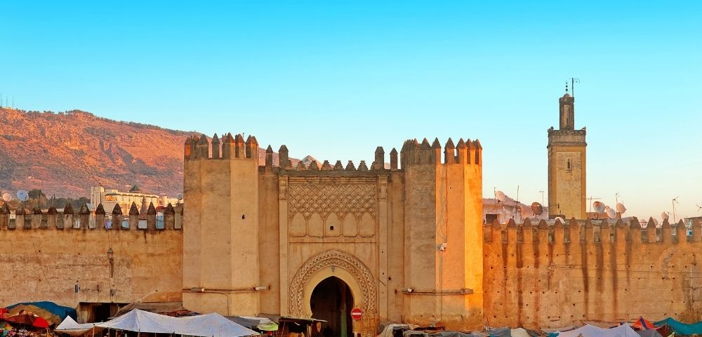 A historical gate of a fortified city with stone walls, surrounded by a market area.