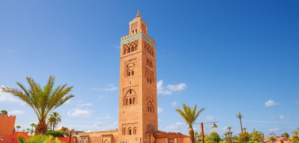 Koutoubia Mosque in Marrakech, Morocco, with a clear blue sky and palm trees in the foreground.
