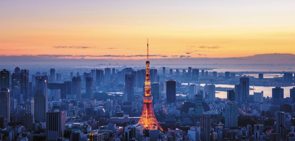A panoramic view of a dense city skyline at dusk, with a brightly lit iconic tower in the center.