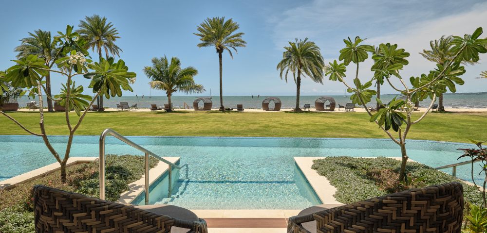 Tropical resort pool overlooking a sandy beach and ocean, framed by palms and lounge chairs, creating a serene, sunny getaway.