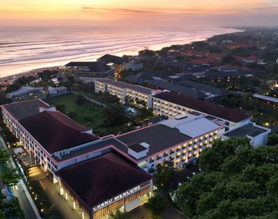 Aerial view of a resort complex with multiple buildings, a beach, and the ocean at sunset.