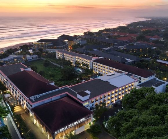 Aerial view of a resort complex with multiple buildings, a beach, and the ocean at sunset.