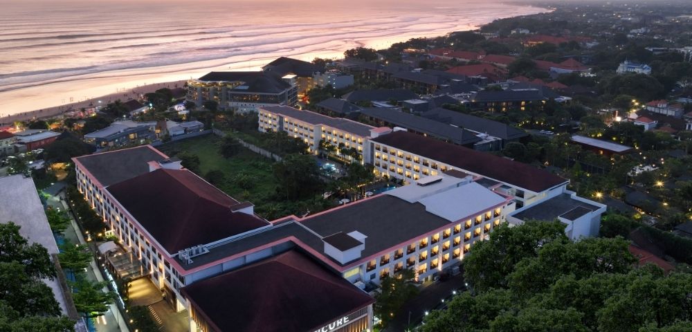 Aerial view of a resort complex with multiple buildings, a beach, and the ocean at sunset.