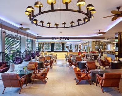 Spacious, modern hotel lobby with hanging pod chairs, leather armchairs, and a bar area in the background.