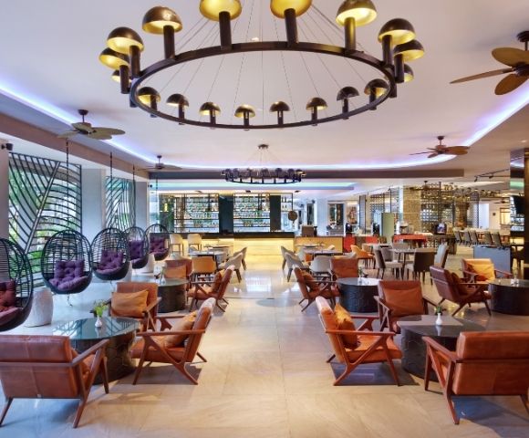 Spacious, modern hotel lobby with hanging pod chairs, leather armchairs, and a bar area in the background.