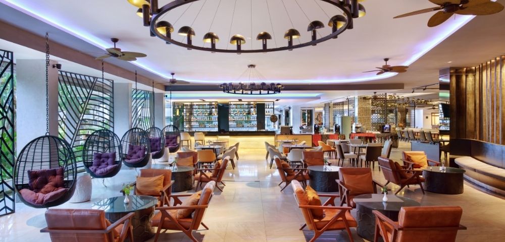 Spacious, modern hotel lobby with hanging pod chairs, leather armchairs, and a bar area in the background.