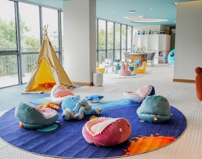 Bright children's playroom with a teepee tent, plush sea creature cushions, colorful chairs, and large windows letting in natural light.