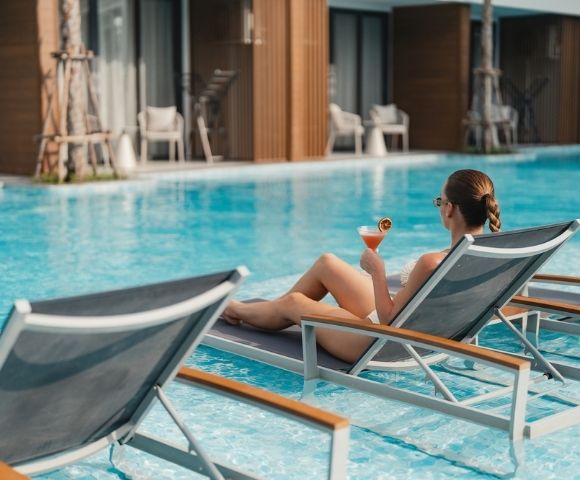 A woman lounging by a pool while holding a cocktail.