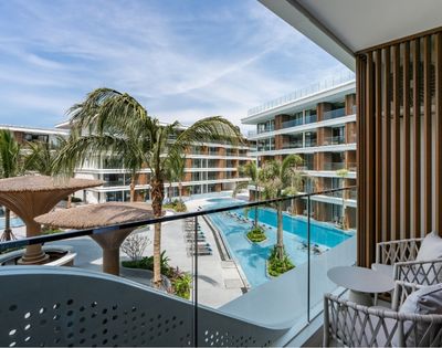 A view from a balcony overlooking a pool area surrounded by palm trees and modern hotel architecture.