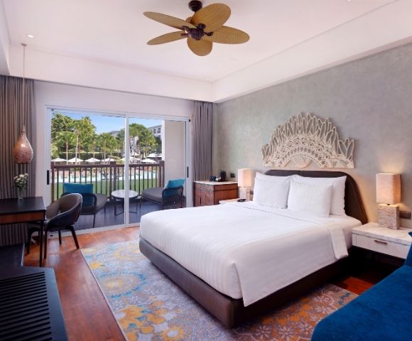 A modern hotel room featuring a large bed, wooden furniture, and a view of a pool through sliding glass doors.