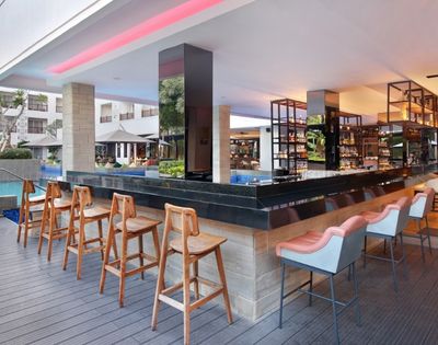 A modern bar area with high stools, located near a pool and surrounded by greenery and seating.