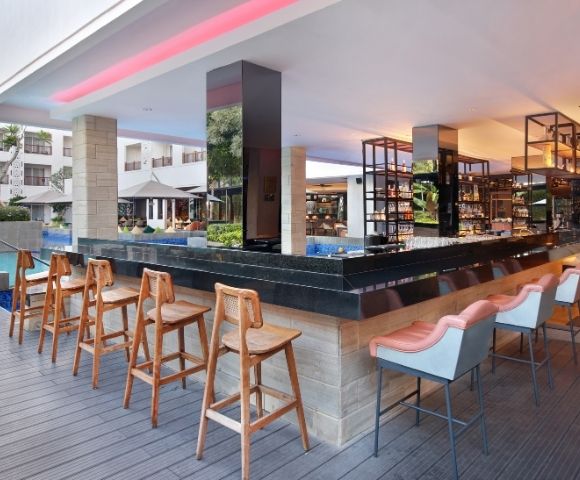 A modern bar area with high stools, located near a pool and surrounded by greenery and seating.