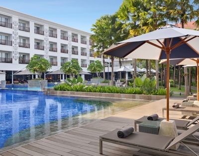 A luxurious hotel pool area with lounge chairs and umbrellas, surrounded by greenery and trees.