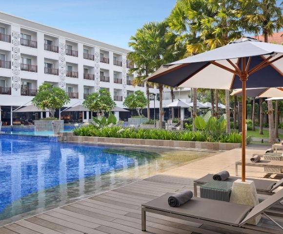A luxurious hotel pool area with lounge chairs and umbrellas, surrounded by greenery and trees.