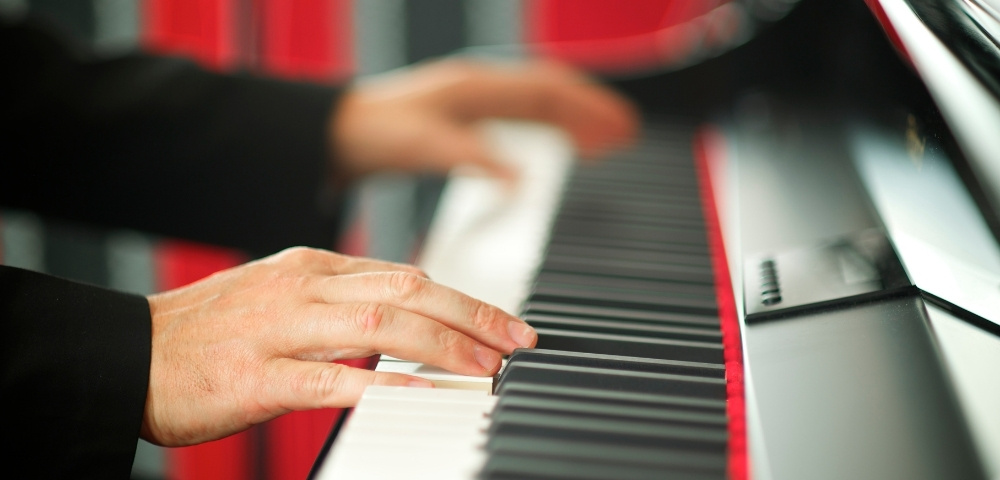Close-up of a pianist’s hands playing black and white keys on a glossy piano, with motion blur suggesting lively, expressive music.