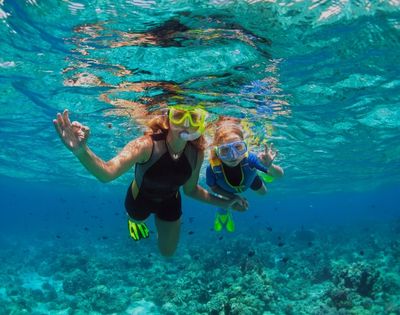 Two individuals in snorkeling gear swim underwater over a coral reef.