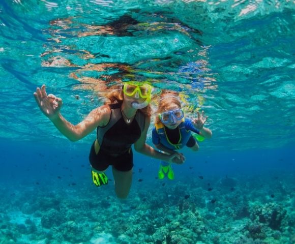 Two individuals in snorkeling gear swim underwater over a coral reef.