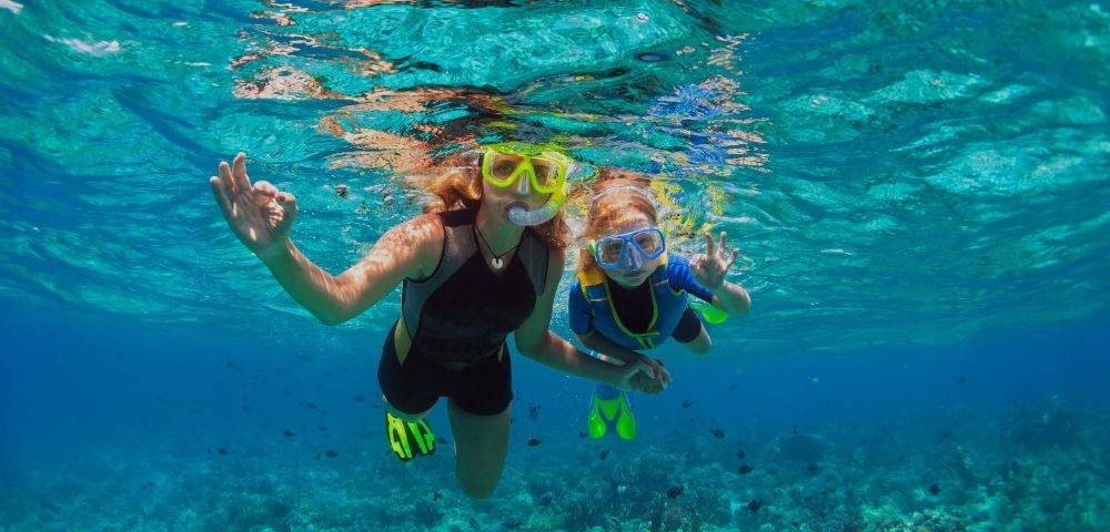 Two individuals in snorkeling gear swim underwater over a coral reef.